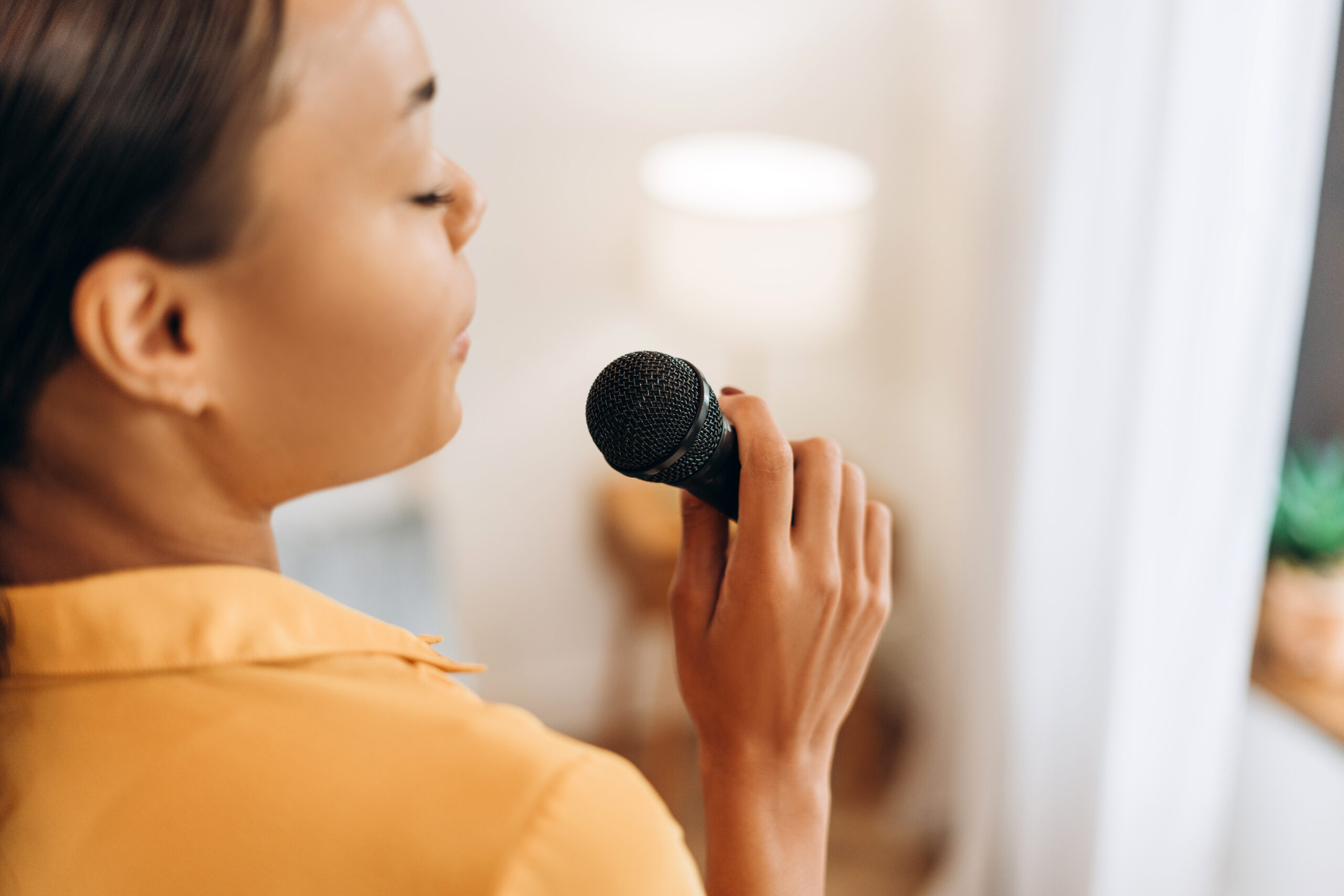 Beautiful, happy, young African American woman singing, holding microphone, copy space, back view. Hobby concept
