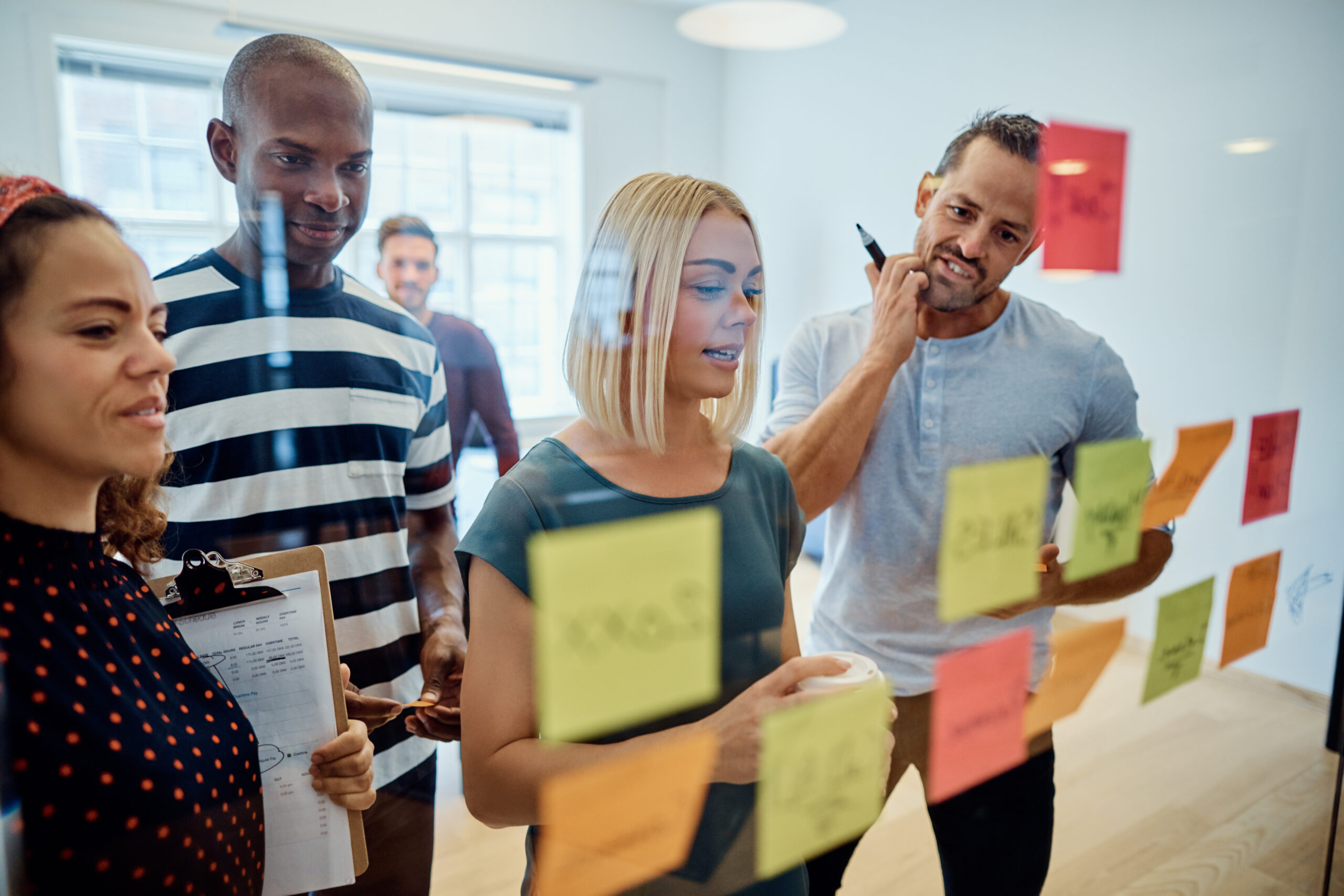 Four people in an office setting organizing post it notes on a glass wall