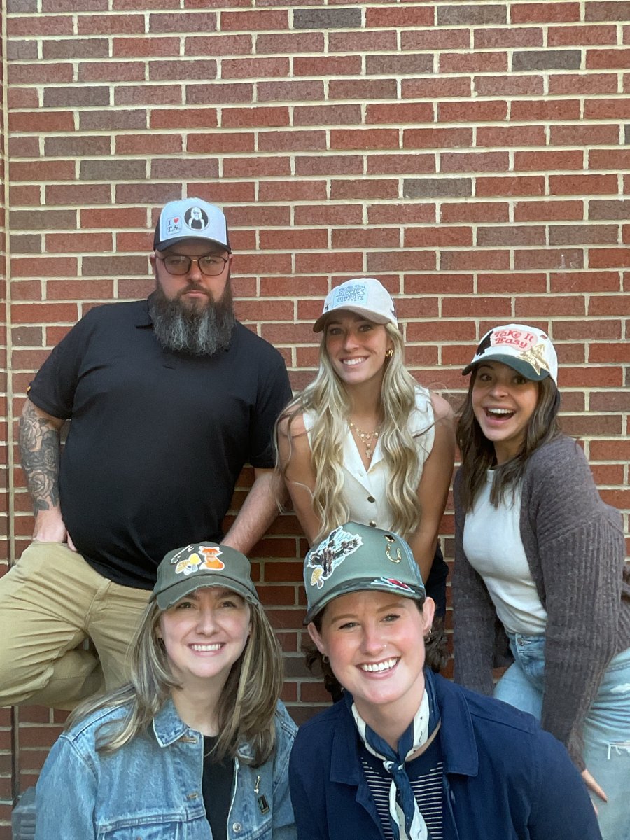 Team members wearing novelty patterned caps posing together against a brick wall