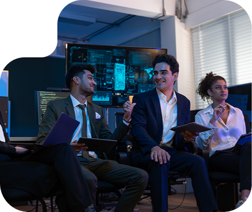 Three people talking with computers in the background and holding digital tablets