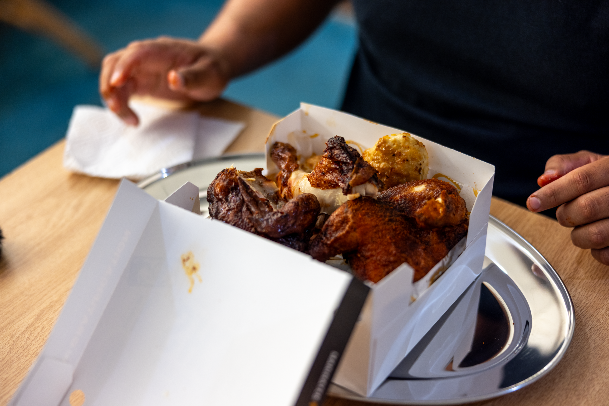 A close-up of an open takeout box filled with Church's Smokehouse Chicken and a biscuit resting on a silver platter.