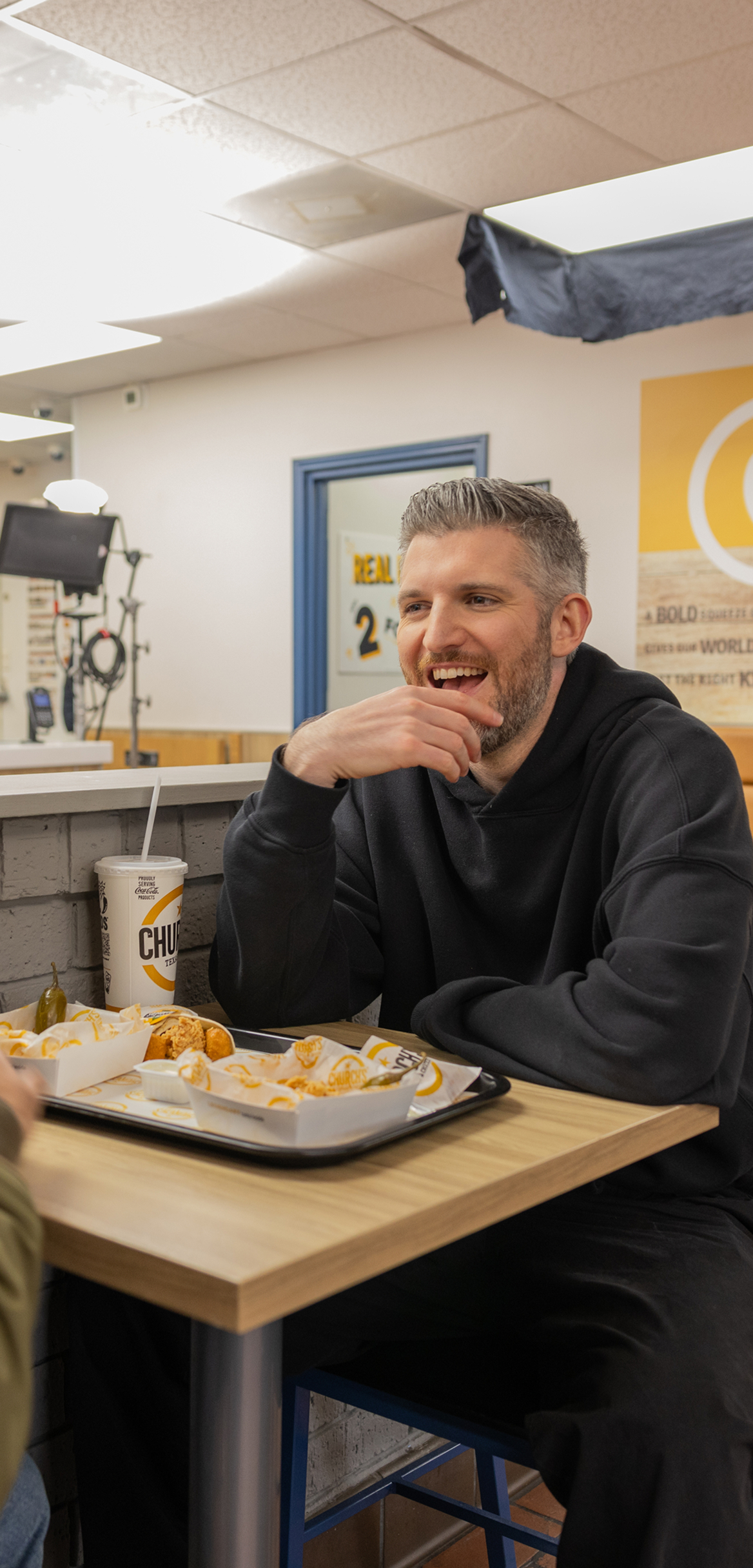 Harry Mack in a black hoodie sitting at a restaurant table with a tray of food and a cup from Church's Texas Chicken.
