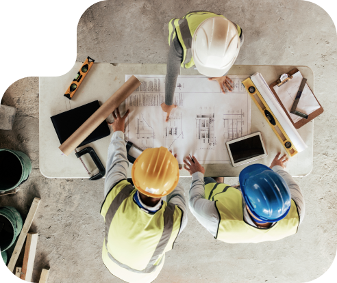 Overhead view of 3 construction workers in hard hats looking at plans on a table