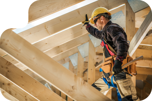 Construction worker in a hard hat holding onto the roof rafters with a hammer