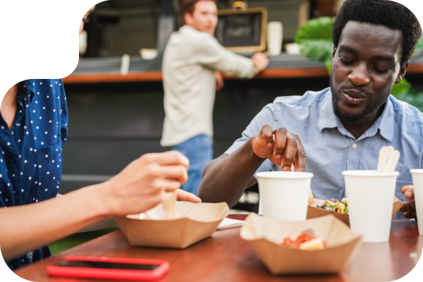 friends eating food at a table with a customer ordering behind them