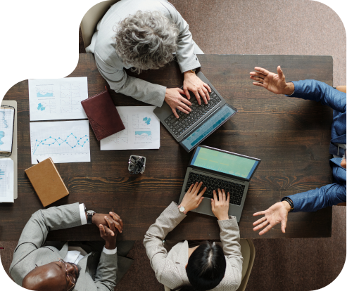 Overhead view of four people in a meeting at a table working on laptops