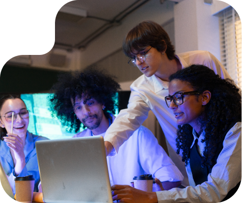 three people sitting in front of a computer screen with one person standing over them pointing at the screen