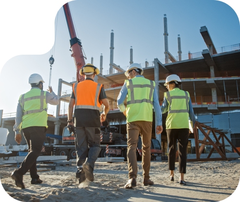 four people in safety vests at a construction site walking towards a building in progress