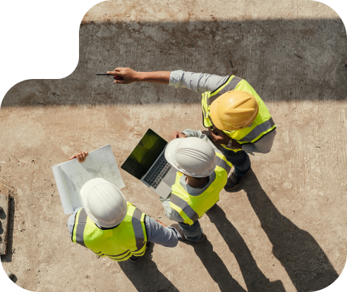 overhead view of 3 people in safety vests and hard hats looking at a computer and plans