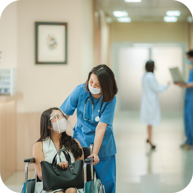 A nurse pushing a patient in a wheelchair. Both are wearing face masks.