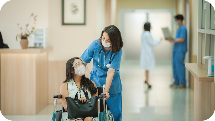 A nurse pushing a patient in a wheelchair. Both are wearing face masks.