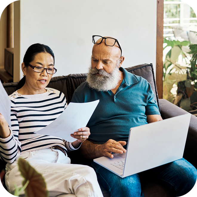 Two people sitting on a couch on looking at papers and the other person working on a laptop