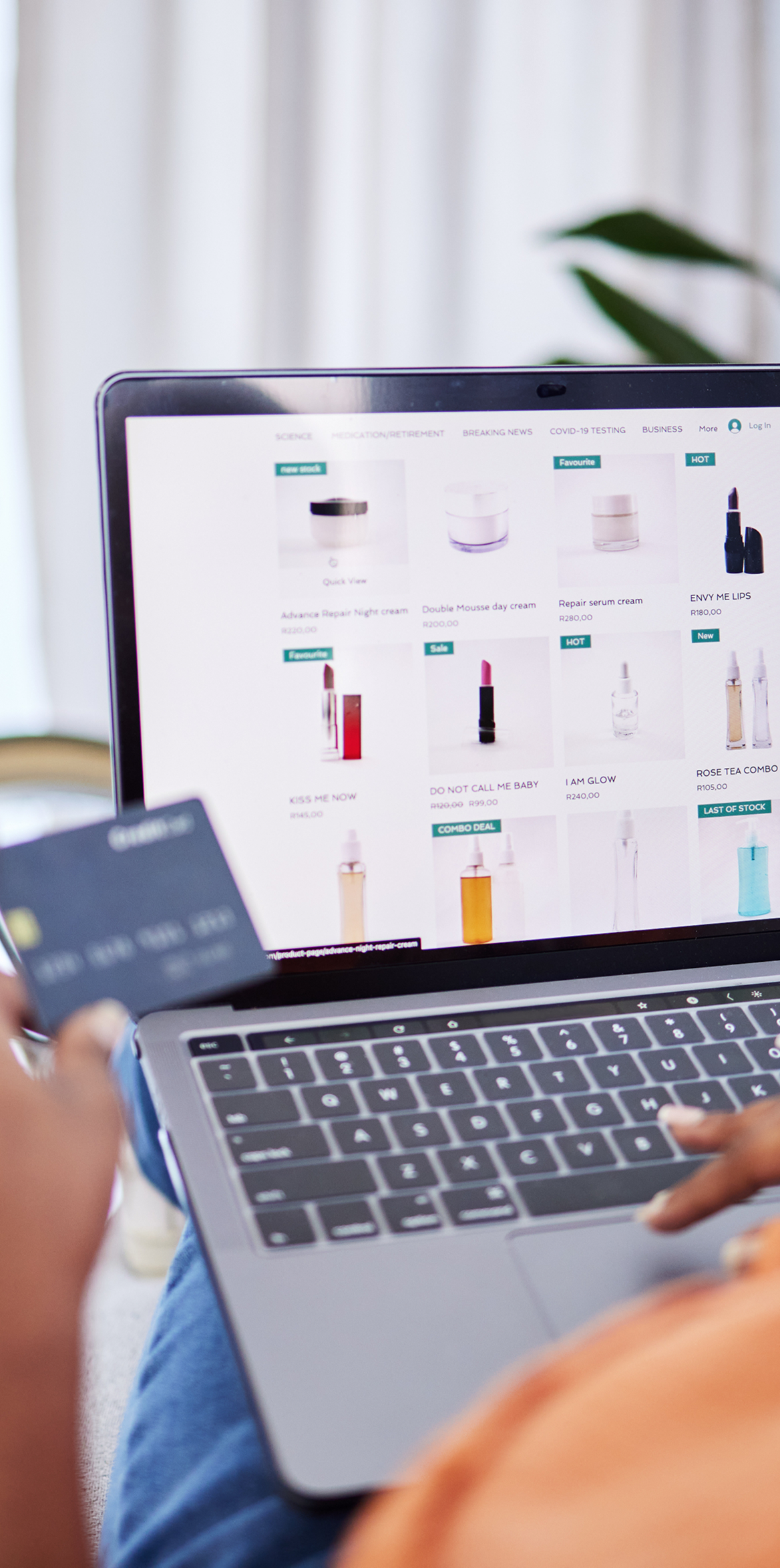 Over-the-shoulder view of a person holding a credit card while browsing an online cosmetics store on a laptop.
