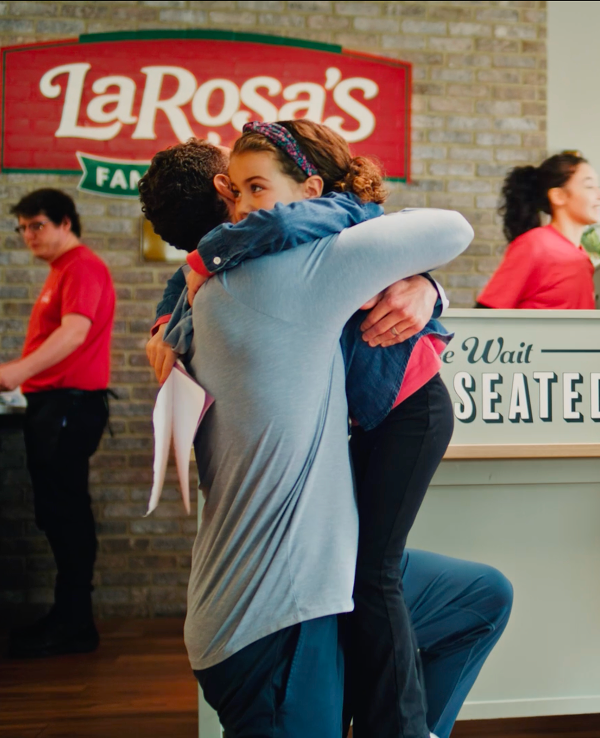 A man hugging a young girl in the lobby of a LaRosa's Family Pizzeria waiting area.