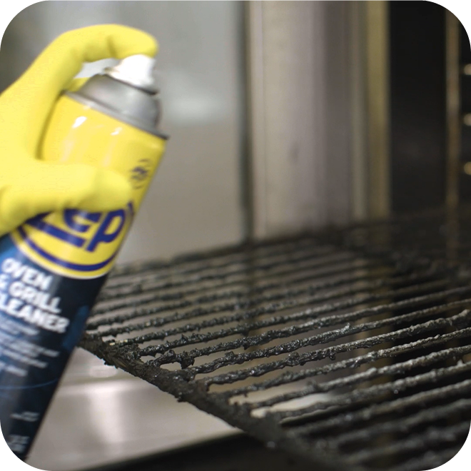 A hand spraying Zep oven cleaner into an opened oven