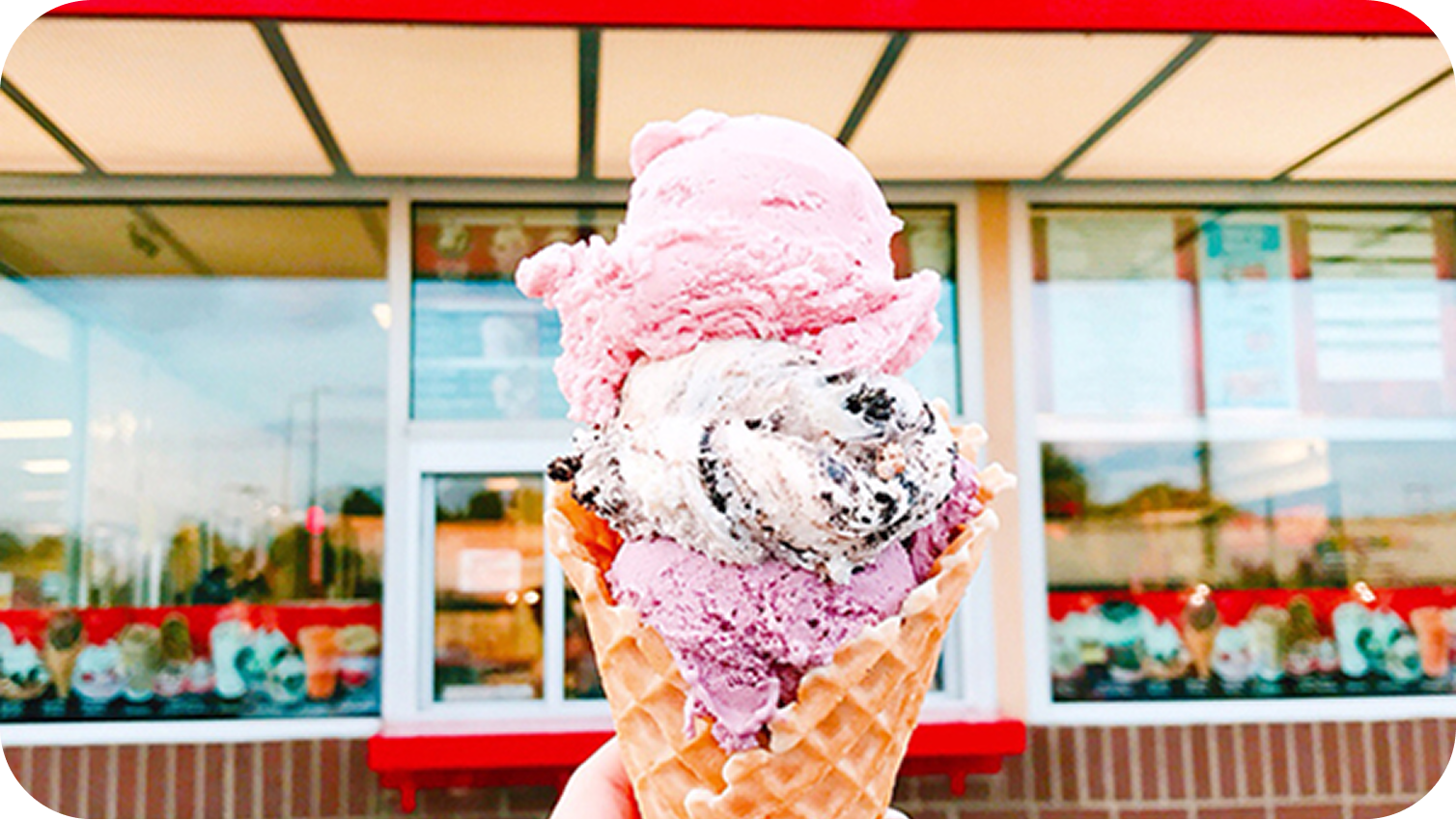 A person holding a three scoop ice cream cone outside of a Bruster's Ice Cream store