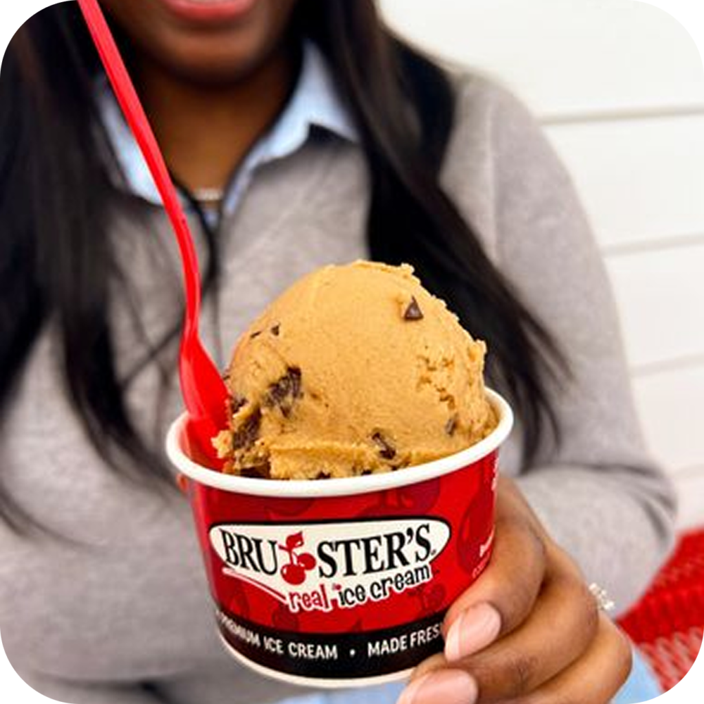A person holding a cup of Bruster's Ice Cream with a red spoon