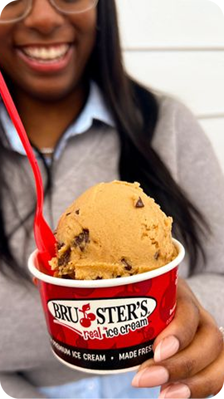 A person holding a cup of Bruster's Ice Cream with a red spoon