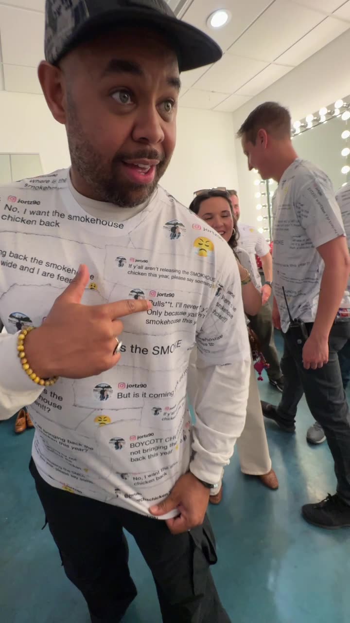 A man wearing a black cap points to his custom white long-sleeve shirt, which is completely covered in printed social media comments from a fan demanding the return of Church's Smokehouse Chicken.
